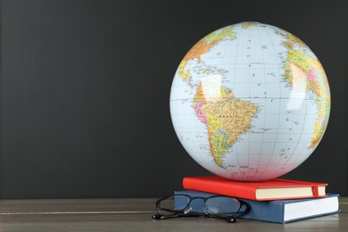 Photo of Globe, books and eyeglasses on wooden table near black chalkboard, space for text. Geography lesson