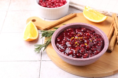 Photo of Tasty cranberry sauce in bowl and ingredients on white tiled table, space for text