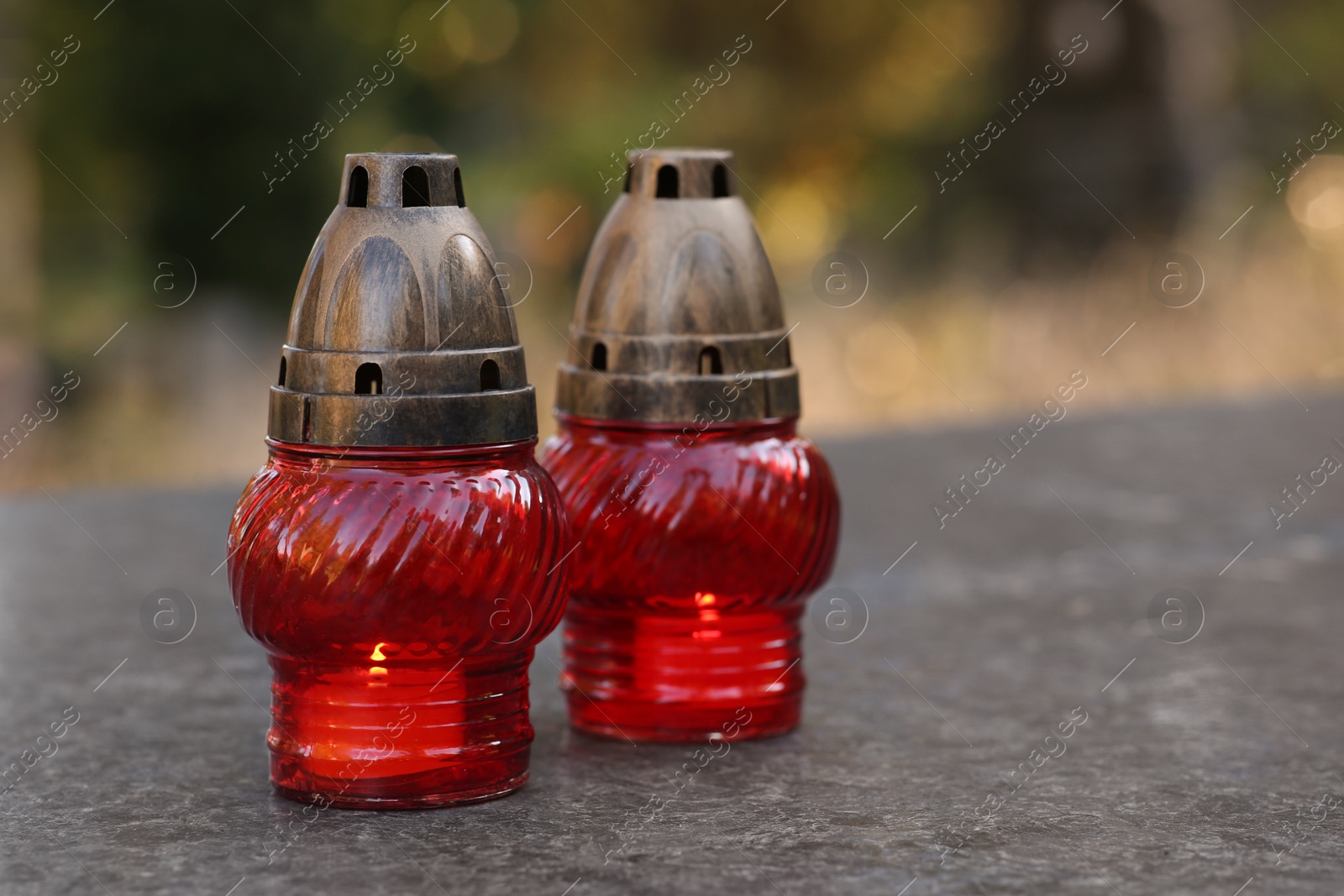 Photo of Red grave lanterns with burning candles on granite surface in cemetery, space for text