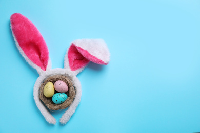 Photo of Headband with bunny ears, painted eggs and space for text on light blue background, flat lay. Easter holiday