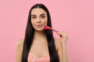 Beautiful woman applying makeup with brush on pink background. Space for text