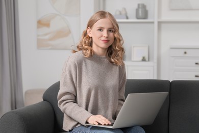 Photo of Beautiful woman with blonde hair using laptop on sofa indoors