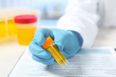 Photo of Laboratory assistant holding container with urine sample for analysis at table, closeup