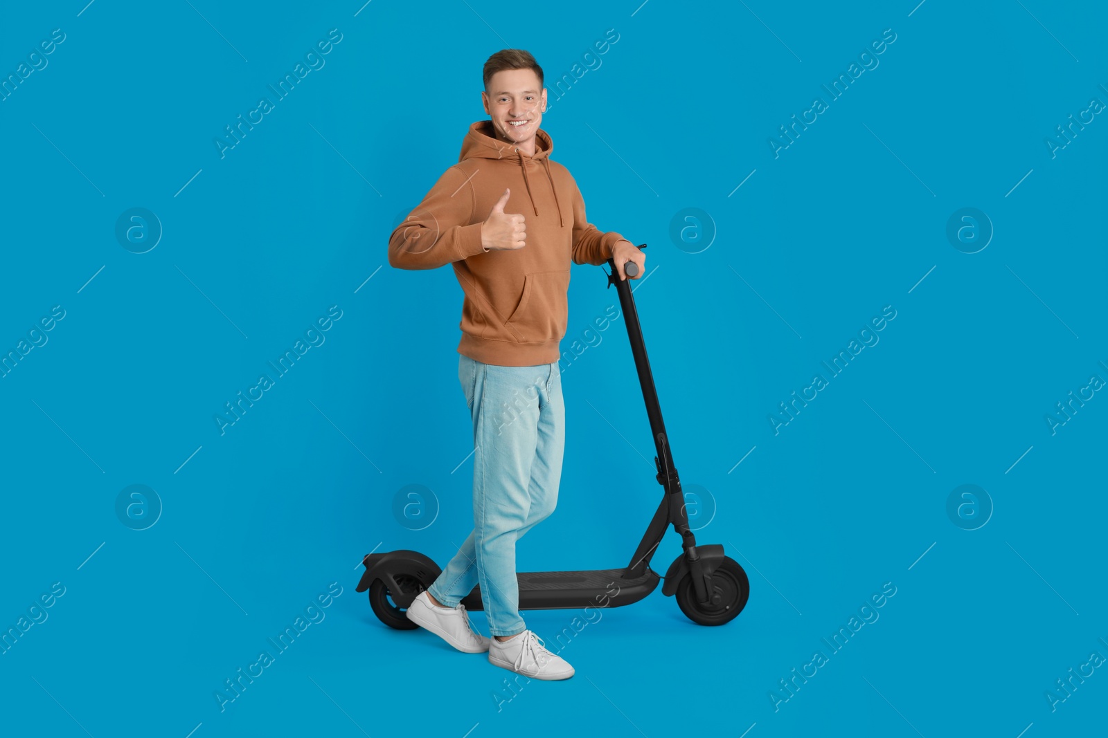 Photo of Happy man with modern electric kick scooter showing thumbs up on light blue background