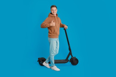 Photo of Happy man with modern electric kick scooter showing thumbs up on light blue background