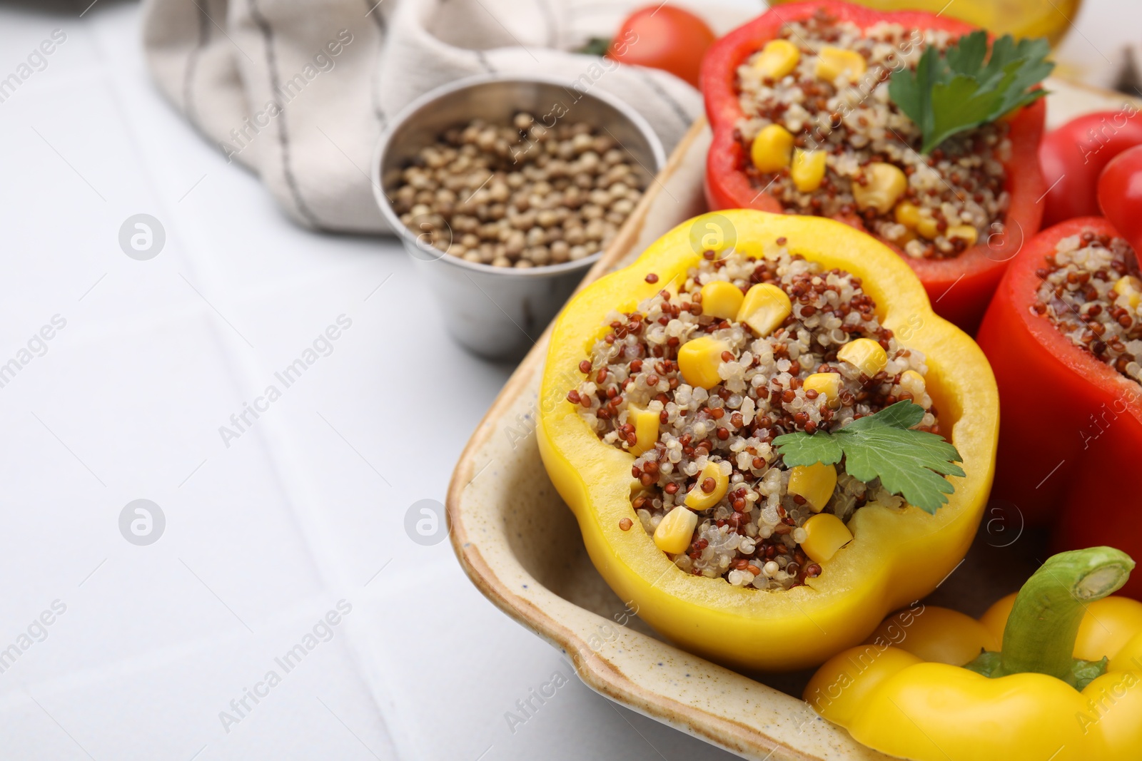 Photo of Quinoa stuffed bell peppers and parsley in baking dish on white tiled table, closeup. Space for text