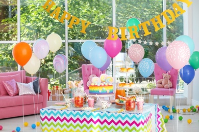 Photo of Bright birthday cake and other treats on table in decorated room