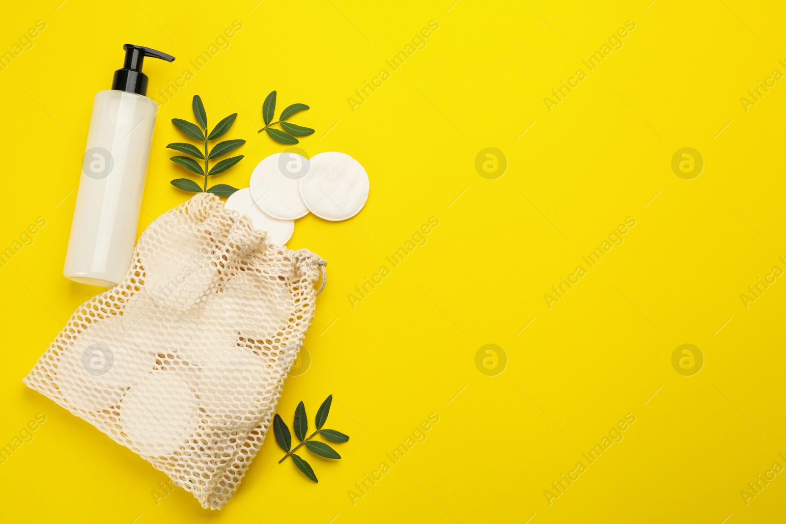 Photo of Cotton pads, leaves, sack and makeup removal product on yellow background, flat lay. Space for text