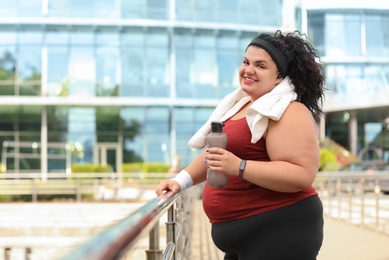 Photo of Beautiful overweight woman in sportswear with bottle and towel outdoors