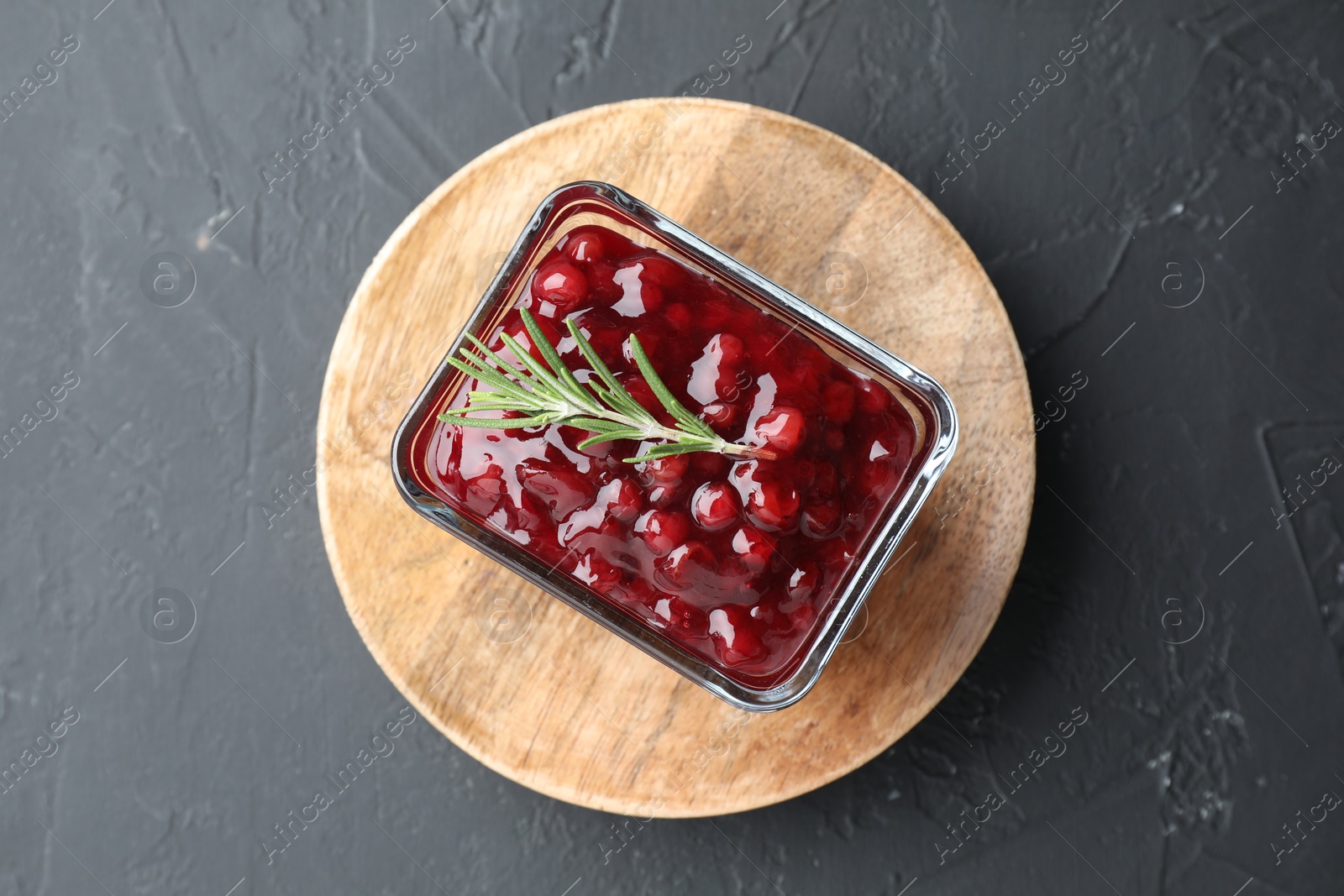 Photo of Fresh cranberry sauce and rosemary in glass bowl on gray textured table, top view