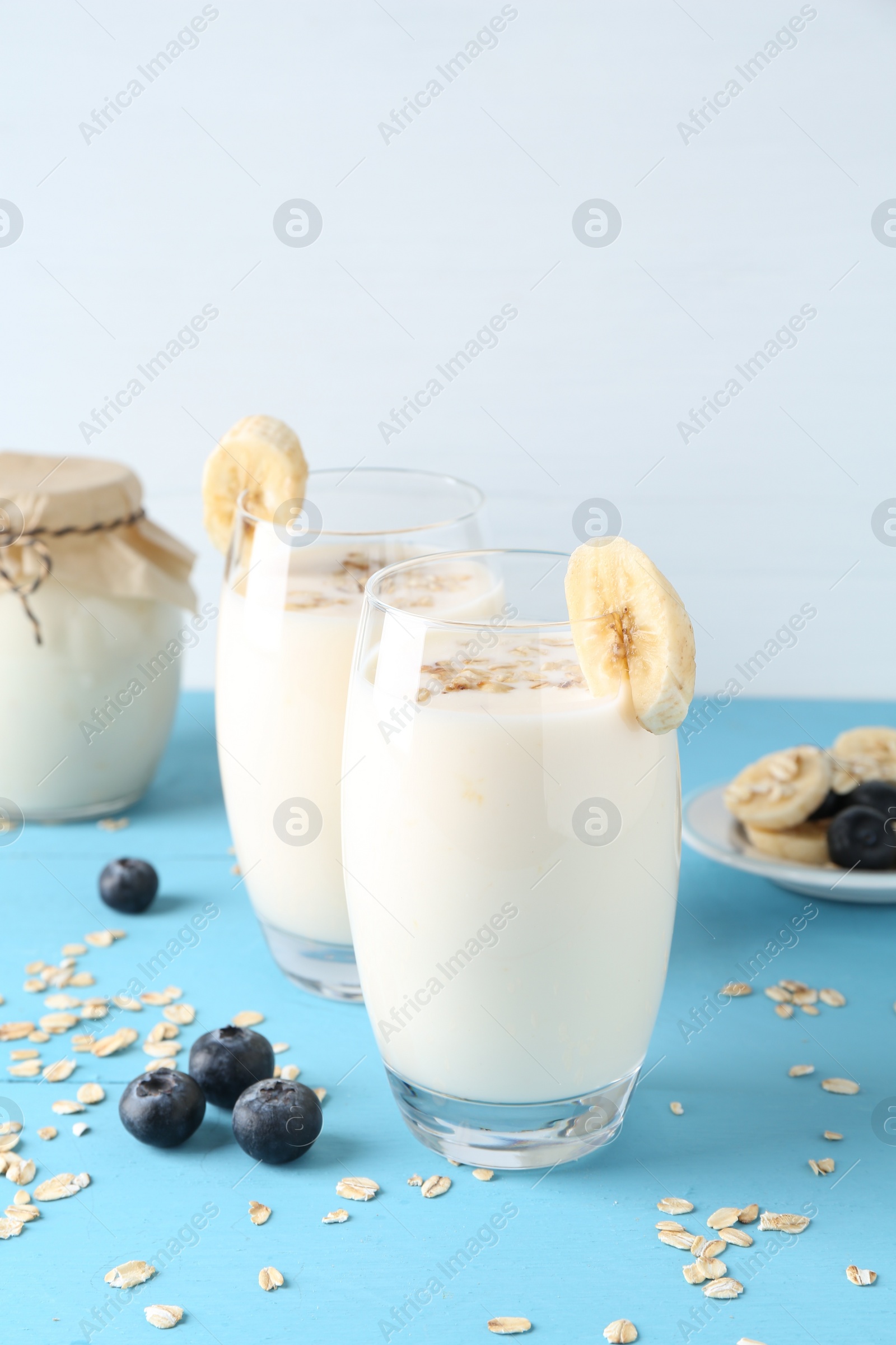 Photo of Tasty yogurt in glasses, oats, banana and blueberries on light blue wooden table