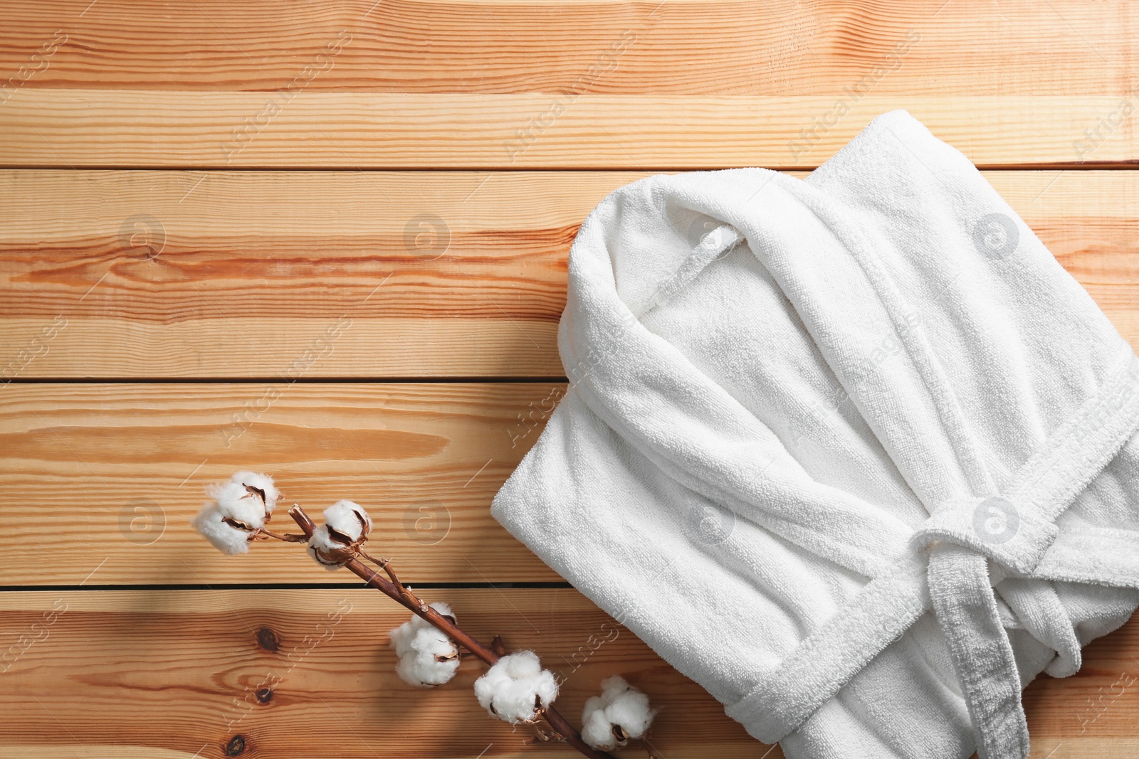 Photo of Clean folded bathrobe and branch of cotton on wooden background, flat lay