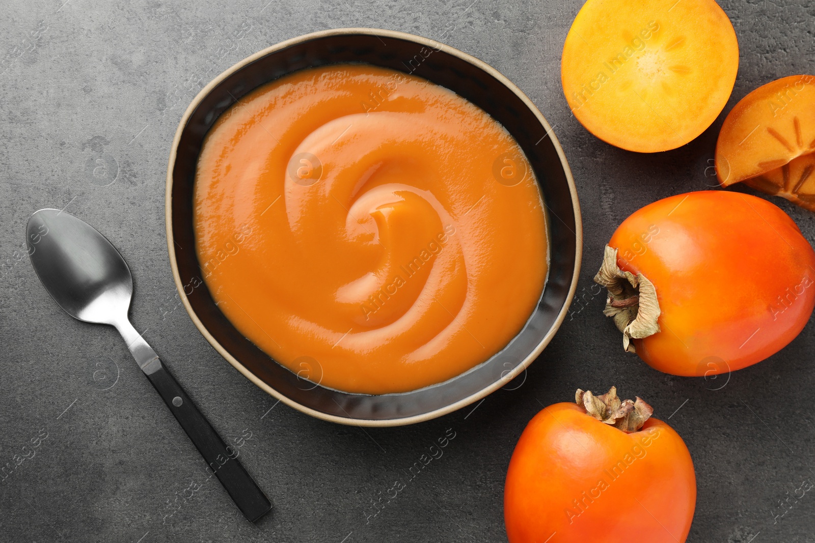 Photo of Delicious persimmon jam in bowl served on gray table, flat lay