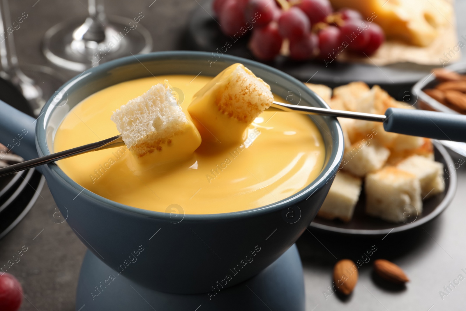 Photo of Pot of tasty cheese fondue and forks with bread pieces at grey table