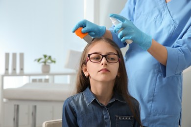 Photo of Doctor using nit comb and spray on girl's hair in clinic. Anti lice treatment