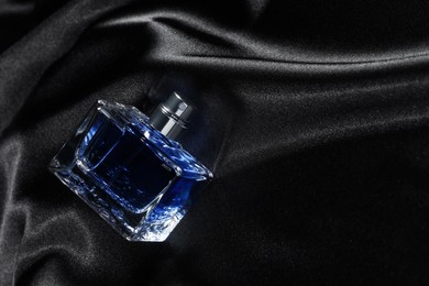 Photo of Luxury men's perfume in bottle on black satin fabric, above view. Space for text