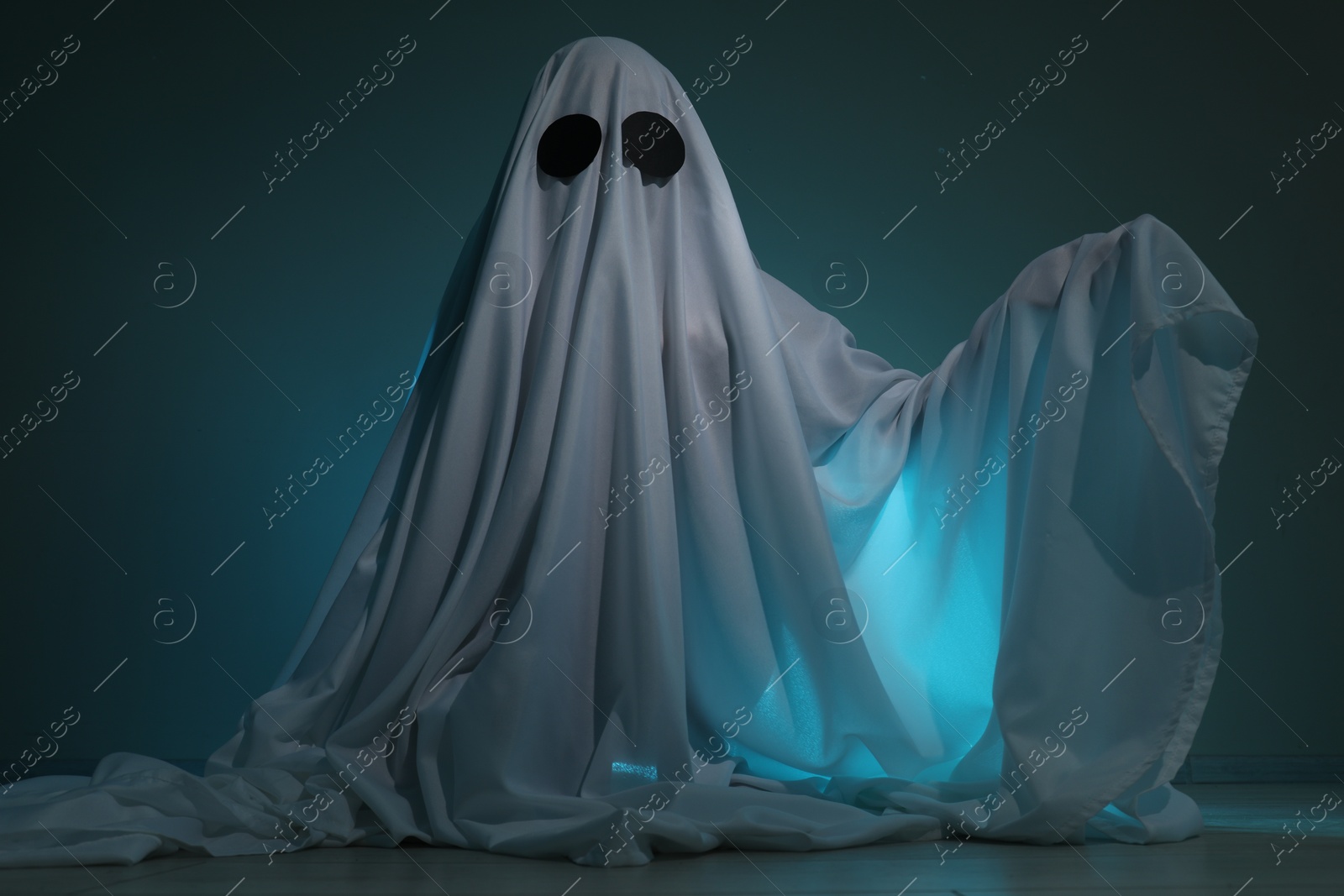 Photo of Creepy ghost. Woman covered with sheet on dark teal background