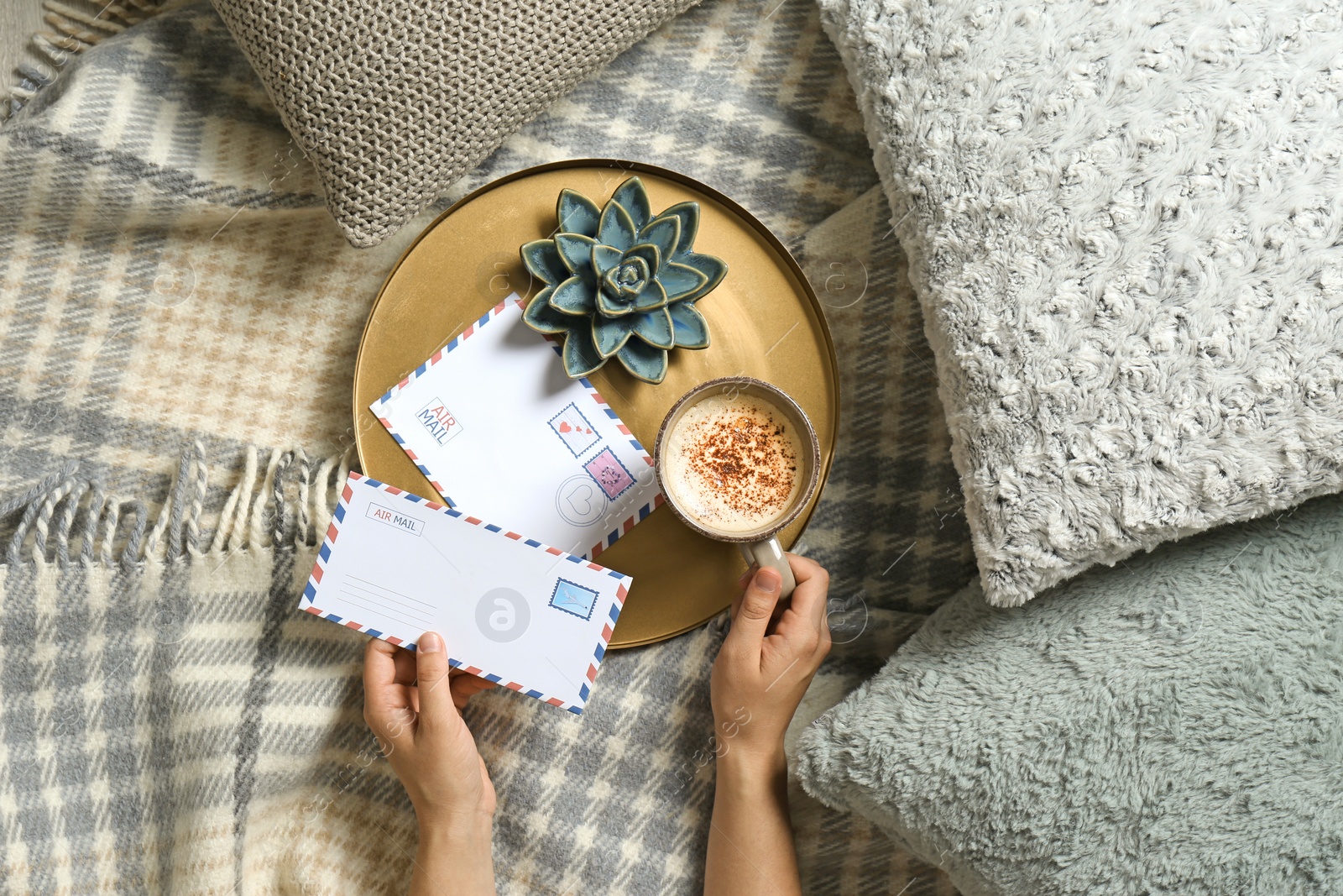 Photo of Woman holding letter while lying on bed with pillows and warm plaid, top view