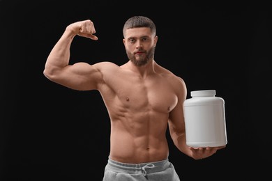 Young man with muscular body holding jar of protein powder on black background