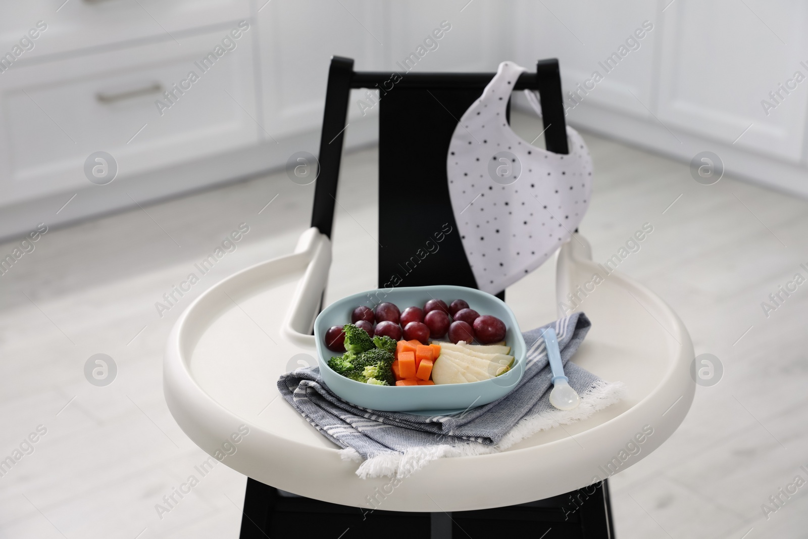 Photo of High chair with food in baby tableware on tray indoors