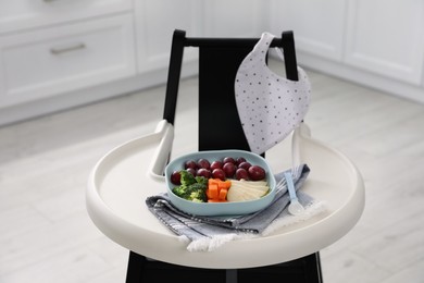 High chair with food in baby tableware on tray indoors