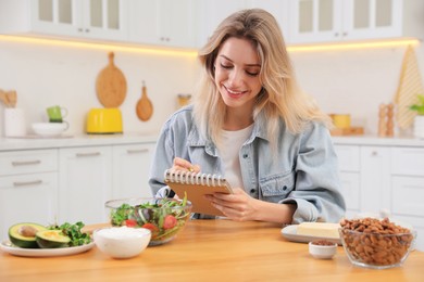 Photo of Woman with notebook and different products at wooden table in kitchen. Keto diet