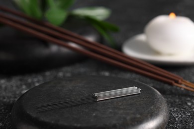 Acupuncture needles and spa stone on black textured table, closeup