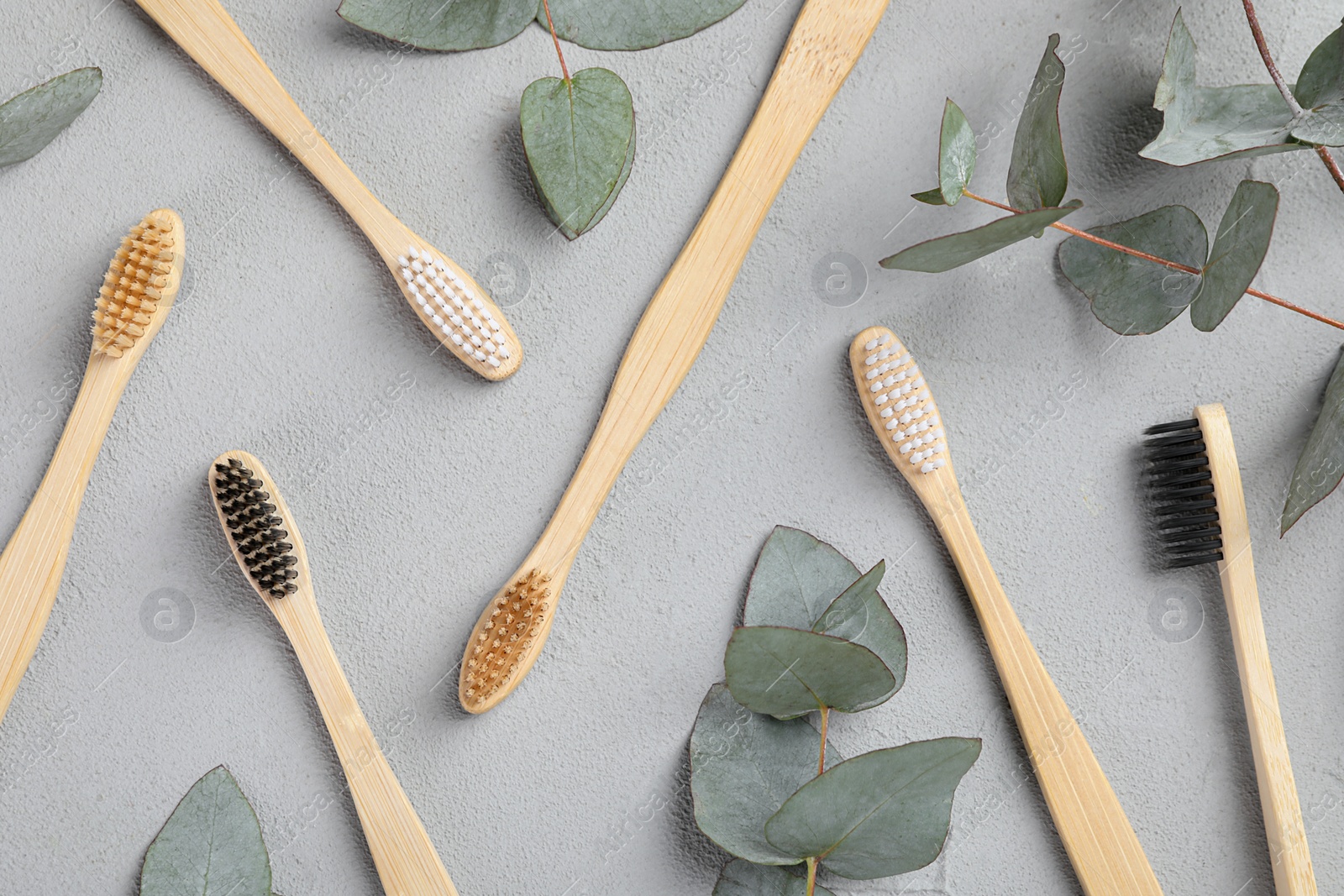 Photo of Many different bamboo toothbrushes and eucalyptus leaves on light grey table, flat lay