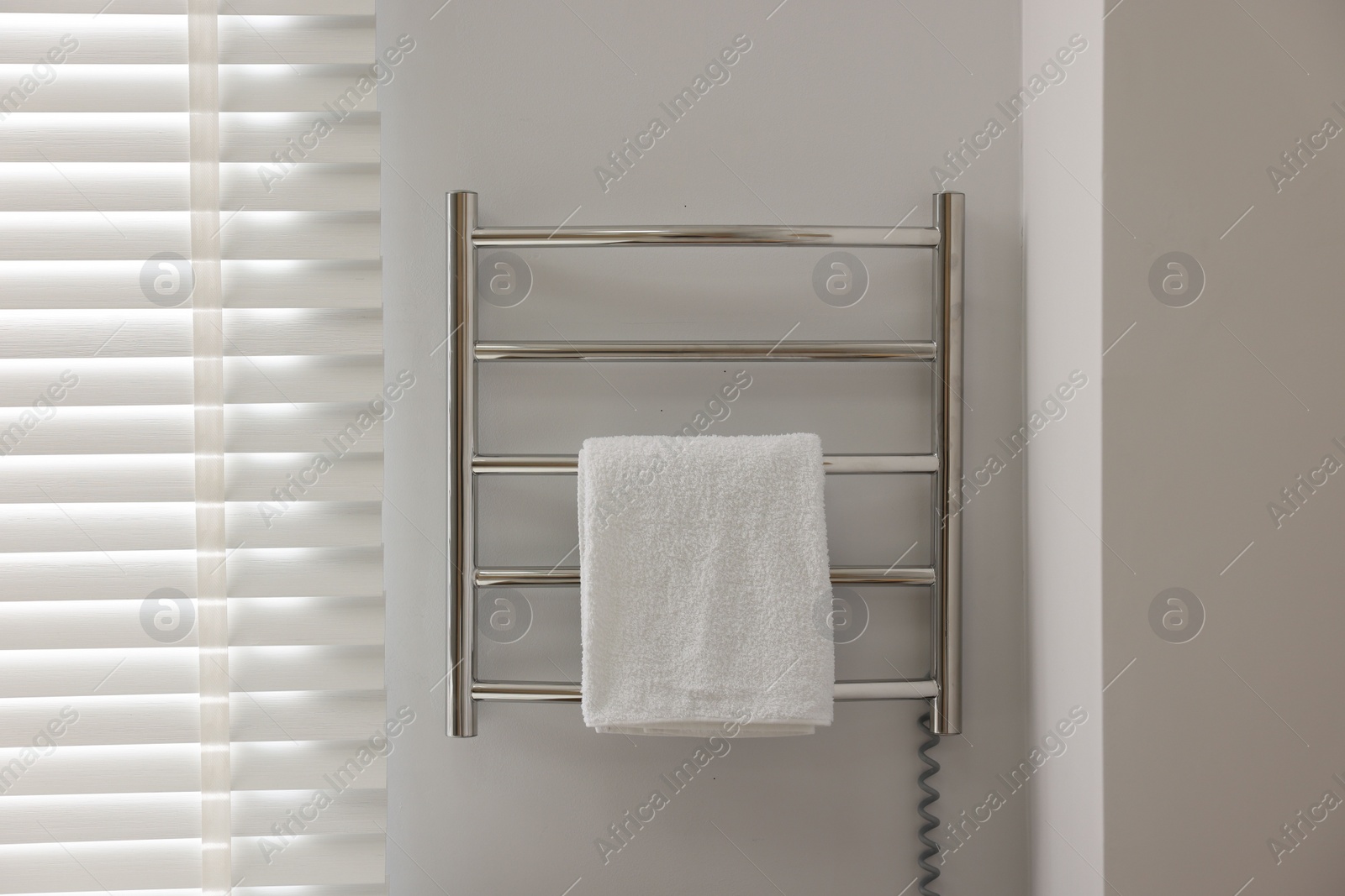 Photo of Heated rail with towel on white wall in bathroom