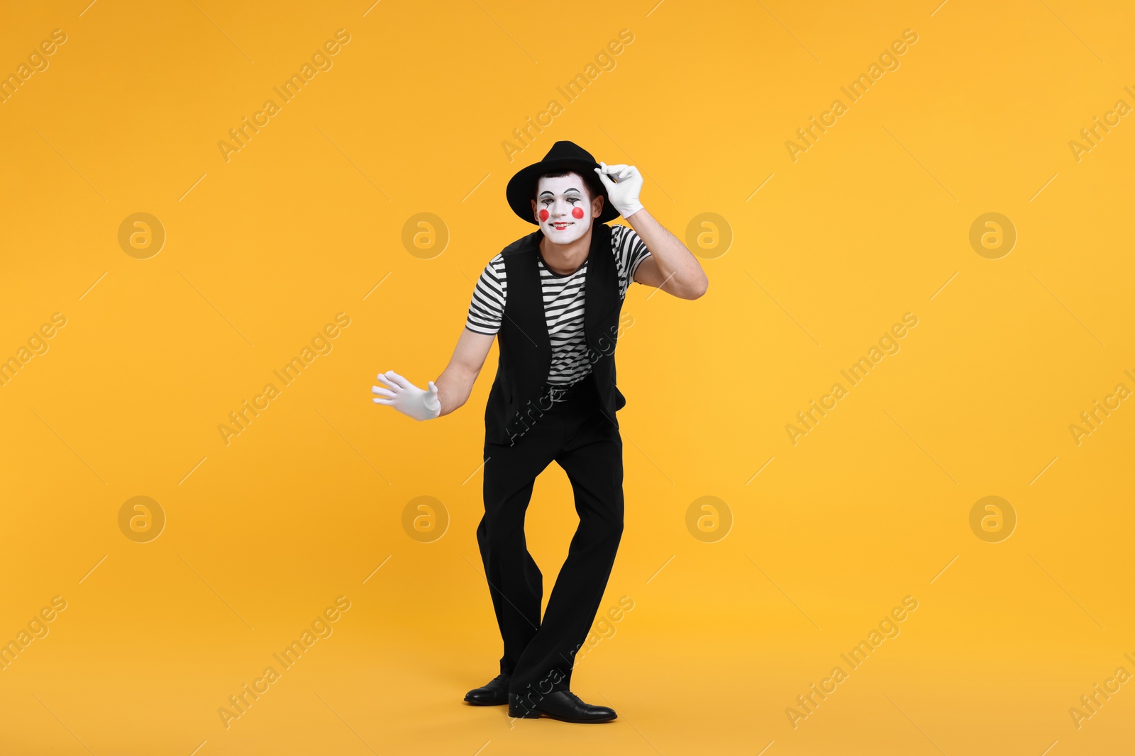 Photo of Funny mime artist in hat posing on orange background