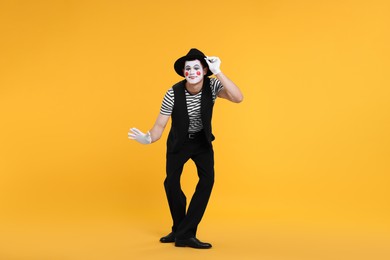 Photo of Funny mime artist in hat posing on orange background