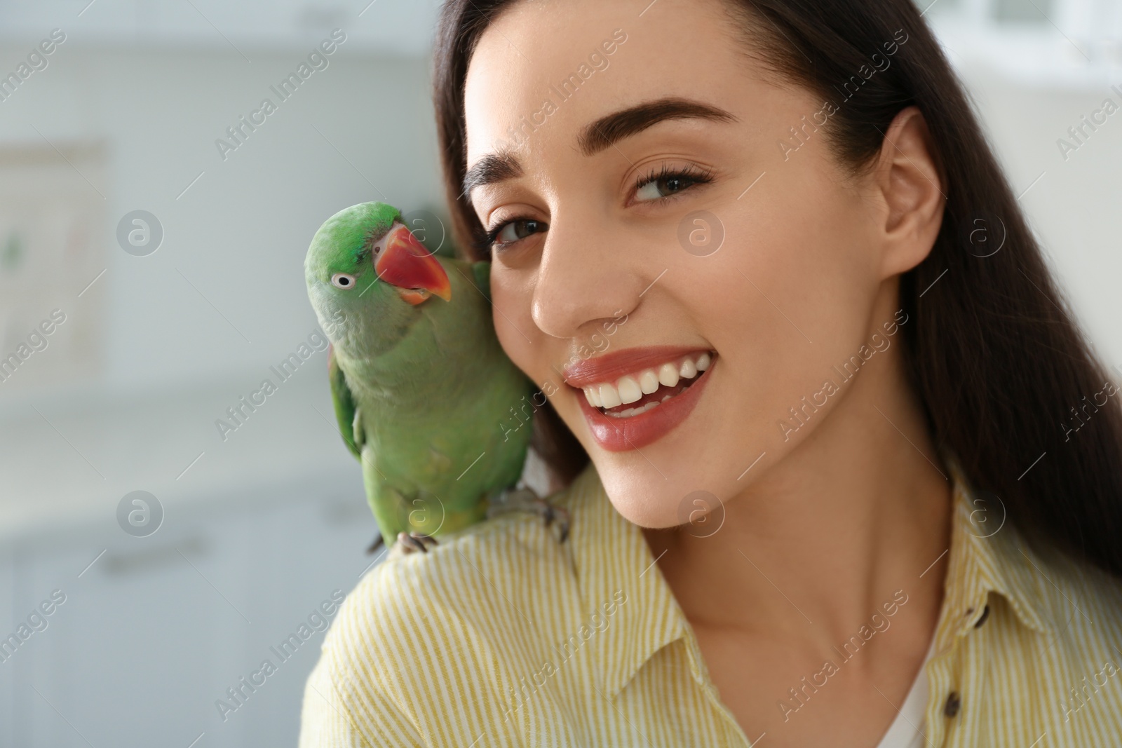 Photo of Young woman with Alexandrine parakeet indoors, closeup. Cute pet