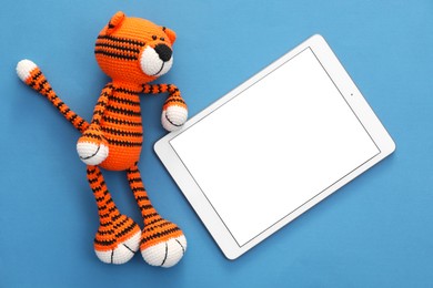 Photo of Modern tablet and toy tiger on blue background, flat lay. Space for text