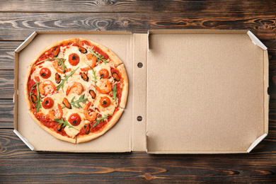 Photo of Delicious seafood pizza in cardboard box on wooden table, top view