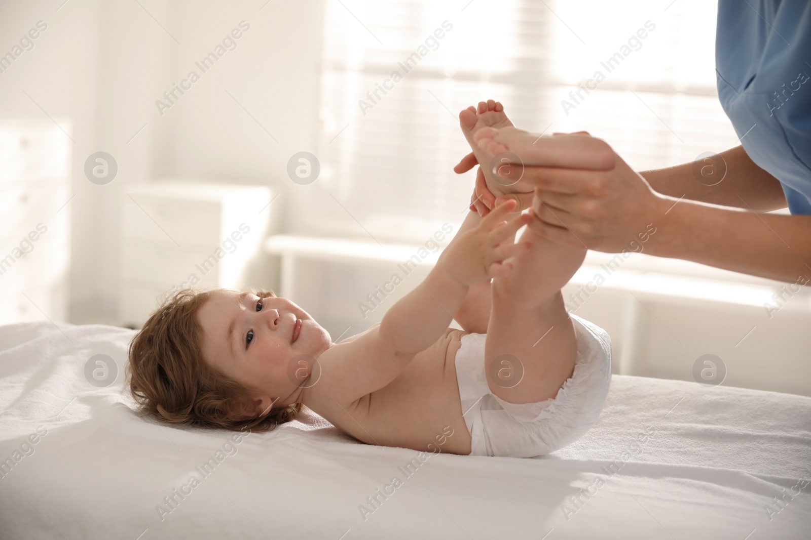 Photo of Orthopedist examining little baby on bed indoors