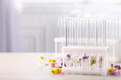 Photo of Test tubes with different flowers on white wooden table, space for text. Essential oil extraction