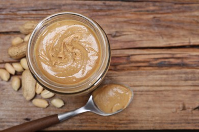 Tasty peanut nut paste in jar and spoon on wooden table, flat lay. Space for text