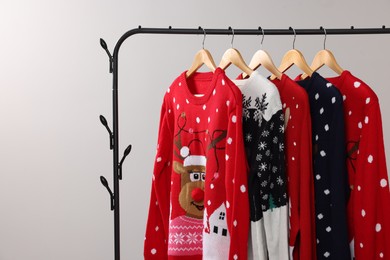 Rack with different Christmas sweaters on light background, space for text