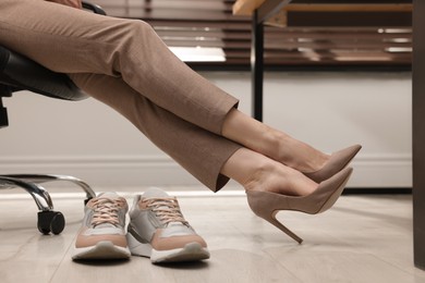 Comfortable sneakers on floor near woman wearing stylish high heeled shoes in office, closeup