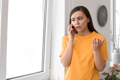 Woman arguing on mobile phone near window at home