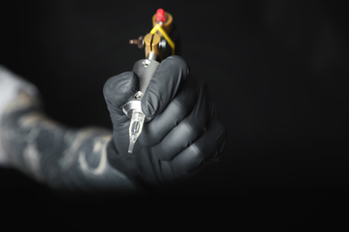 Photo of Tattoo artist with professional machine on black background, closeup