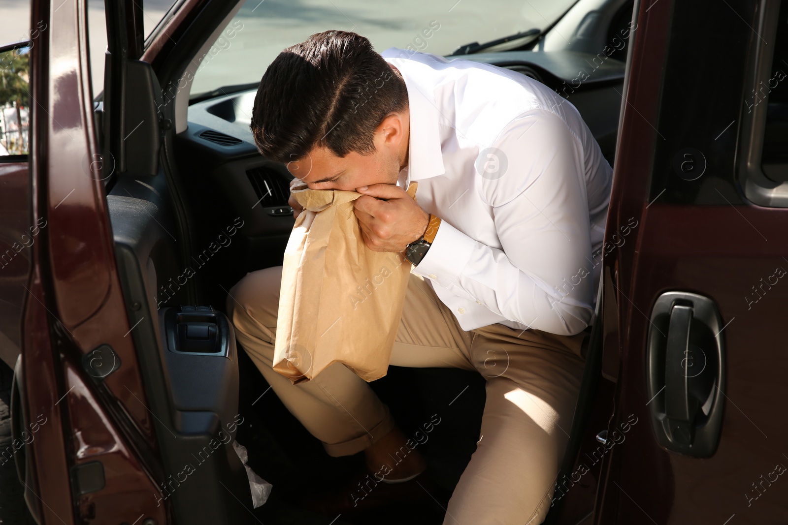 Photo of Man with paper bag suffering from nausea in car