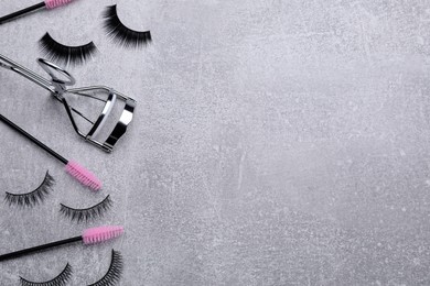 Flat lay composition with false eyelashes, brushes and curler on light grey background. Space for text