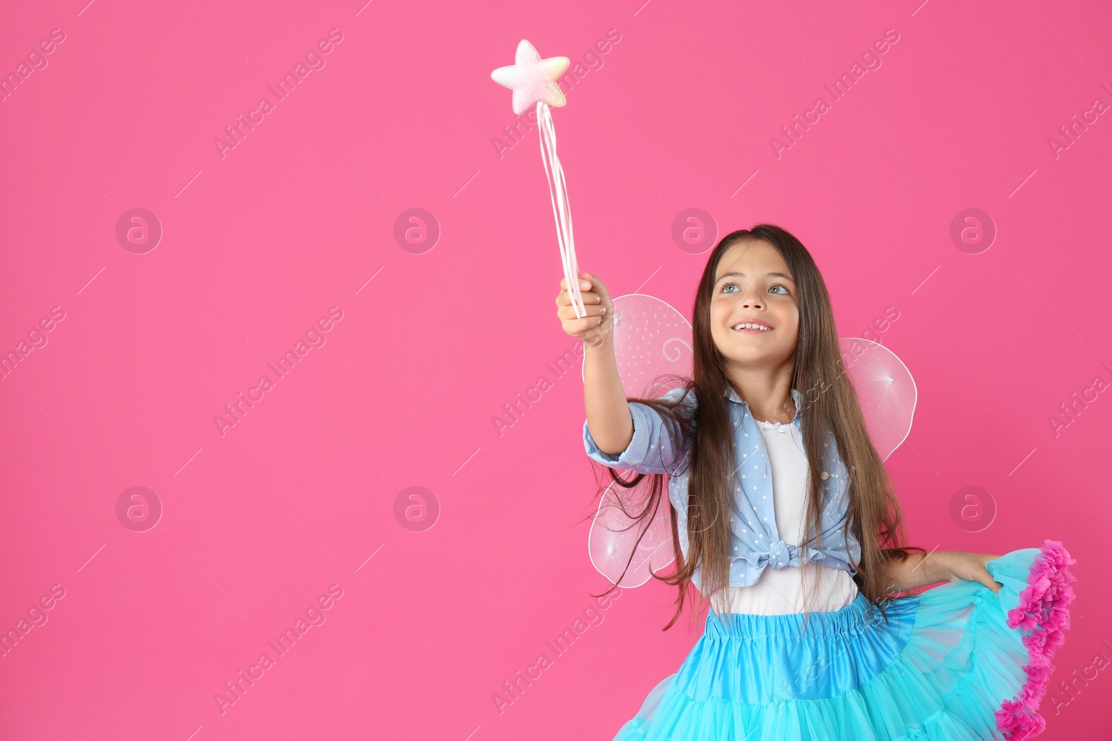 Photo of Cute little girl in fairy costume with wings and magic wand on pink background. Space for text