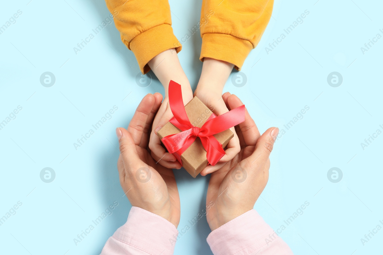 Photo of Mother giving gift box to her child on light blue background, top view