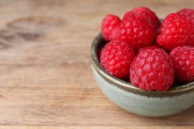 Tasty ripe raspberries in bowl on wooden table, closeup. Space for text