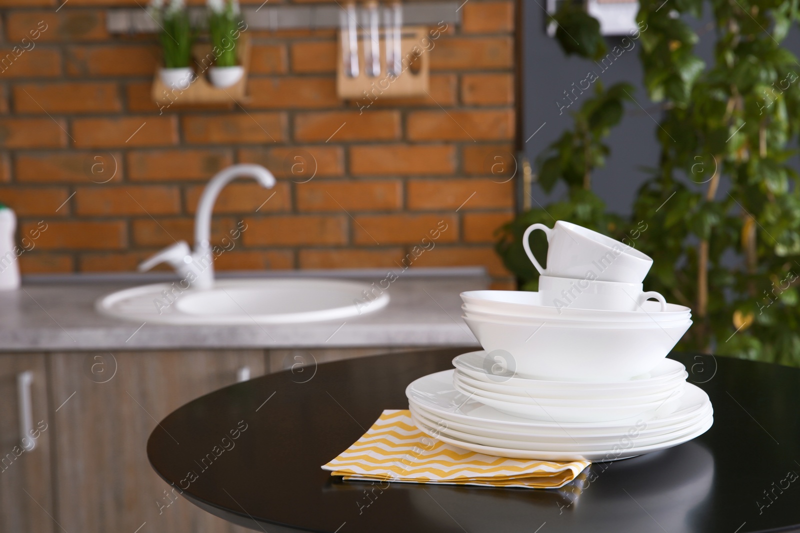 Photo of Stack of clean dishes and cups on table against blurred background. Space for text