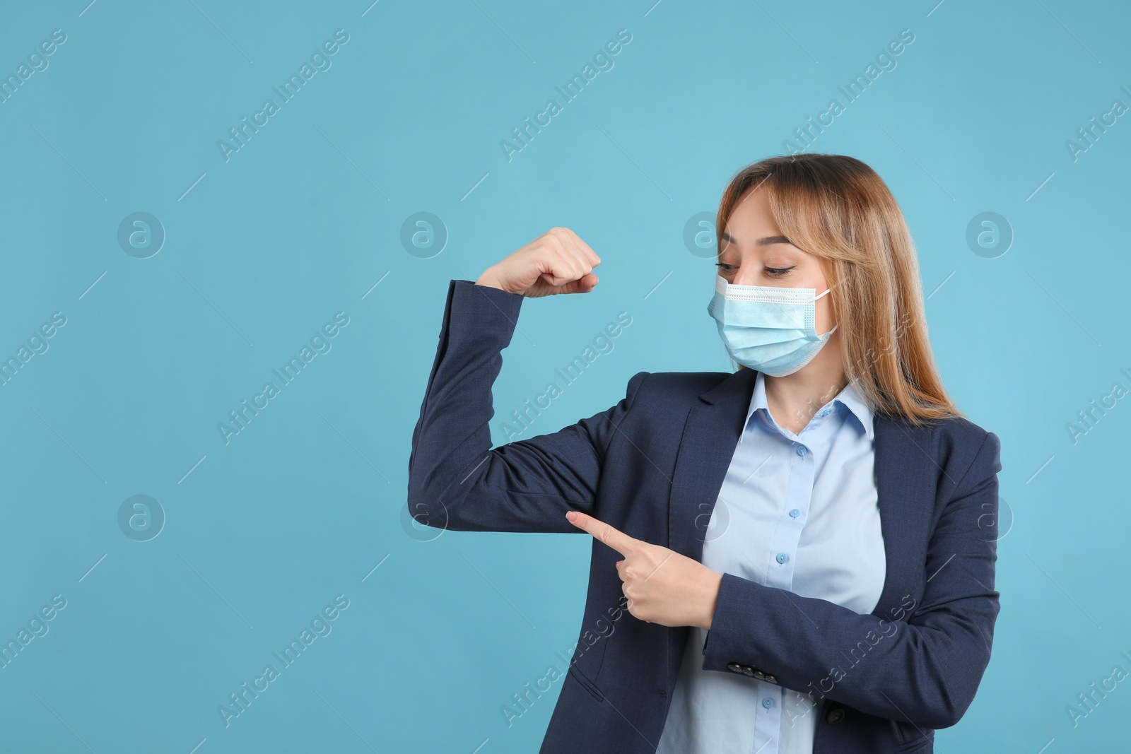 Photo of Businesswoman with protective mask showing muscles on light blue background, space for text. Strong immunity concept