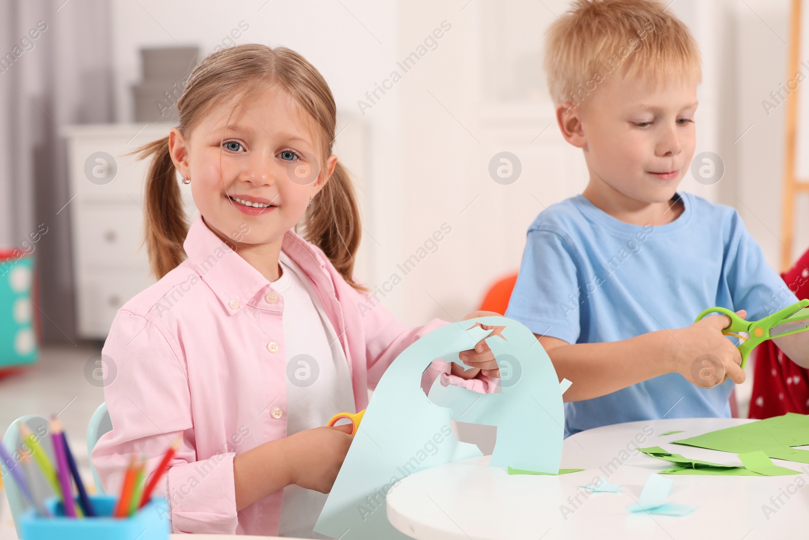 Photo of Cute little children cutting color paper with scissors at desk in kindergarten. Playtime activities