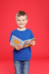 Cute little boy reading book on color background